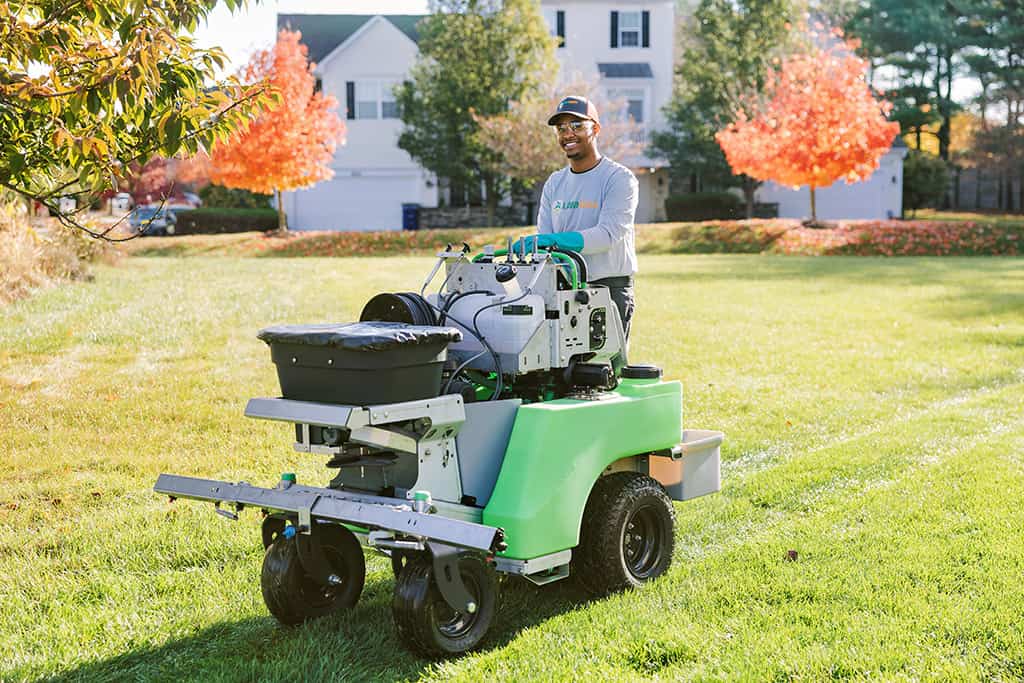 Greenlawn technician with calibrated spreader applying grub control treatment to Columbia lawn, professional equipment visible