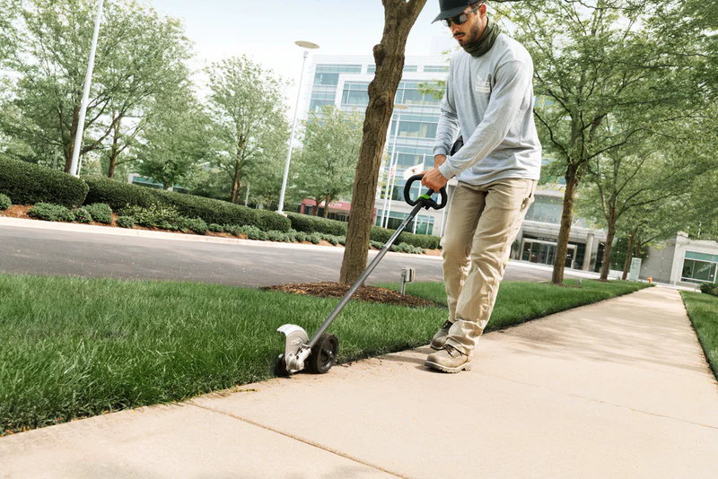 Close-up of commercial power edger cutting clean vertical line along concrete driveway in Columbia showing professional equipment in action