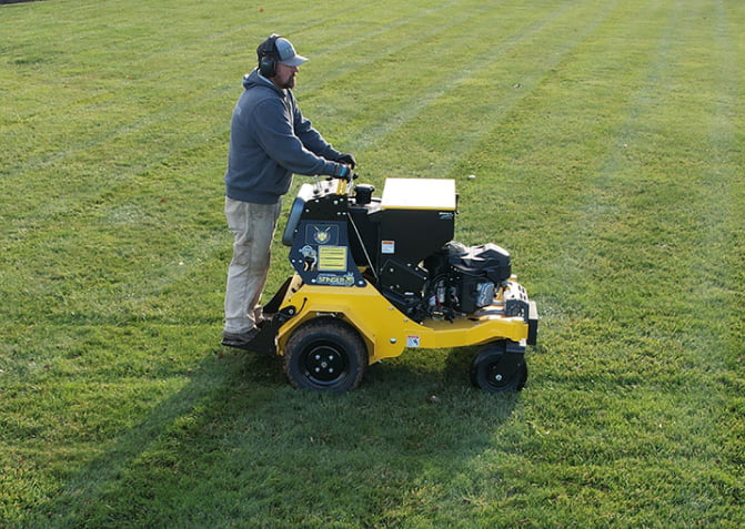 Greenlawn technician spreading grass seed with commercial broadcast spreader over freshly aerated Ellicott City lawn showing soil plugs