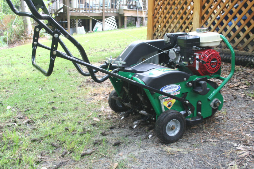 Professional using commercial walk-behind core aerator on Columbia lawn, showing machine in action with soil plugs visible on grass surface behind